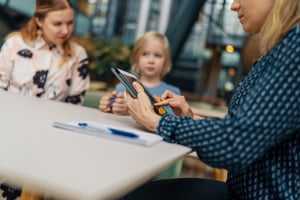 Lapsi ja äiti sosiaalityöntekijän vastaanotolla, sosiaalityöntekijällä tabletti kädessä. 